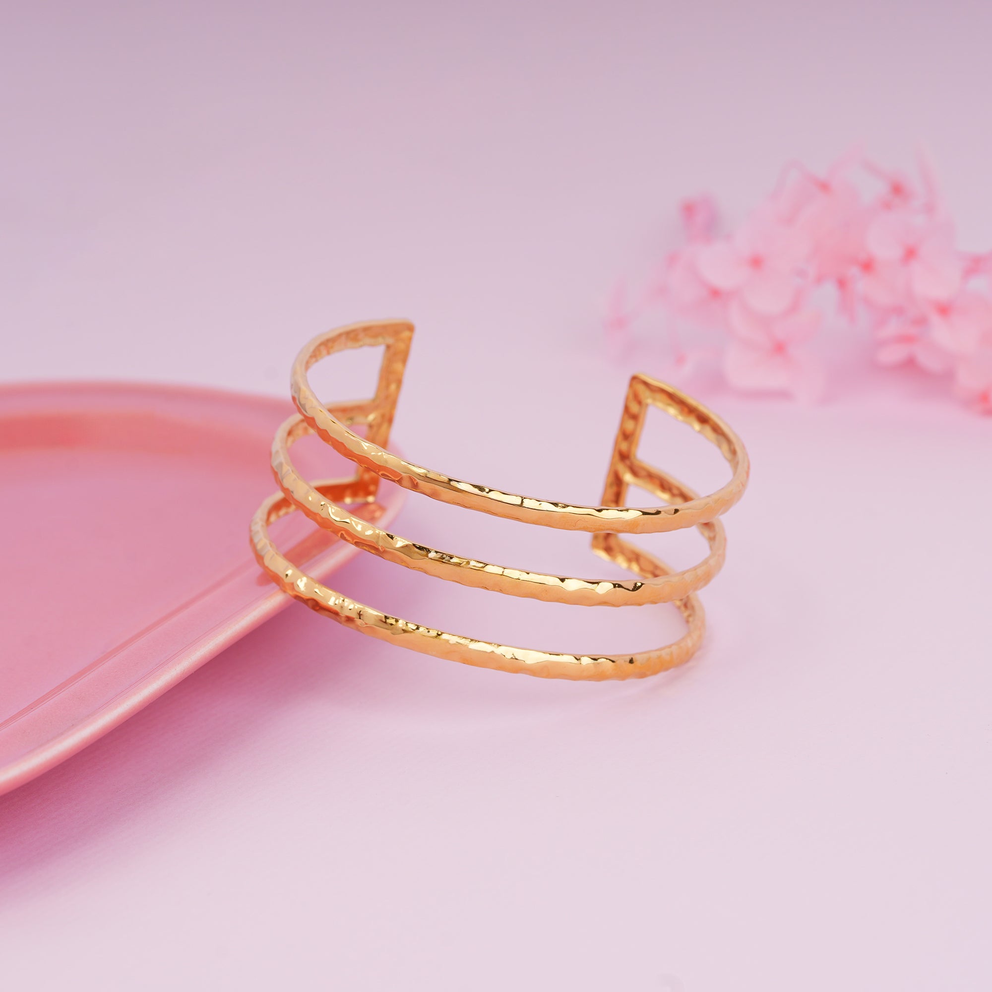Gold bracelet on a pink surface with a soft pink background