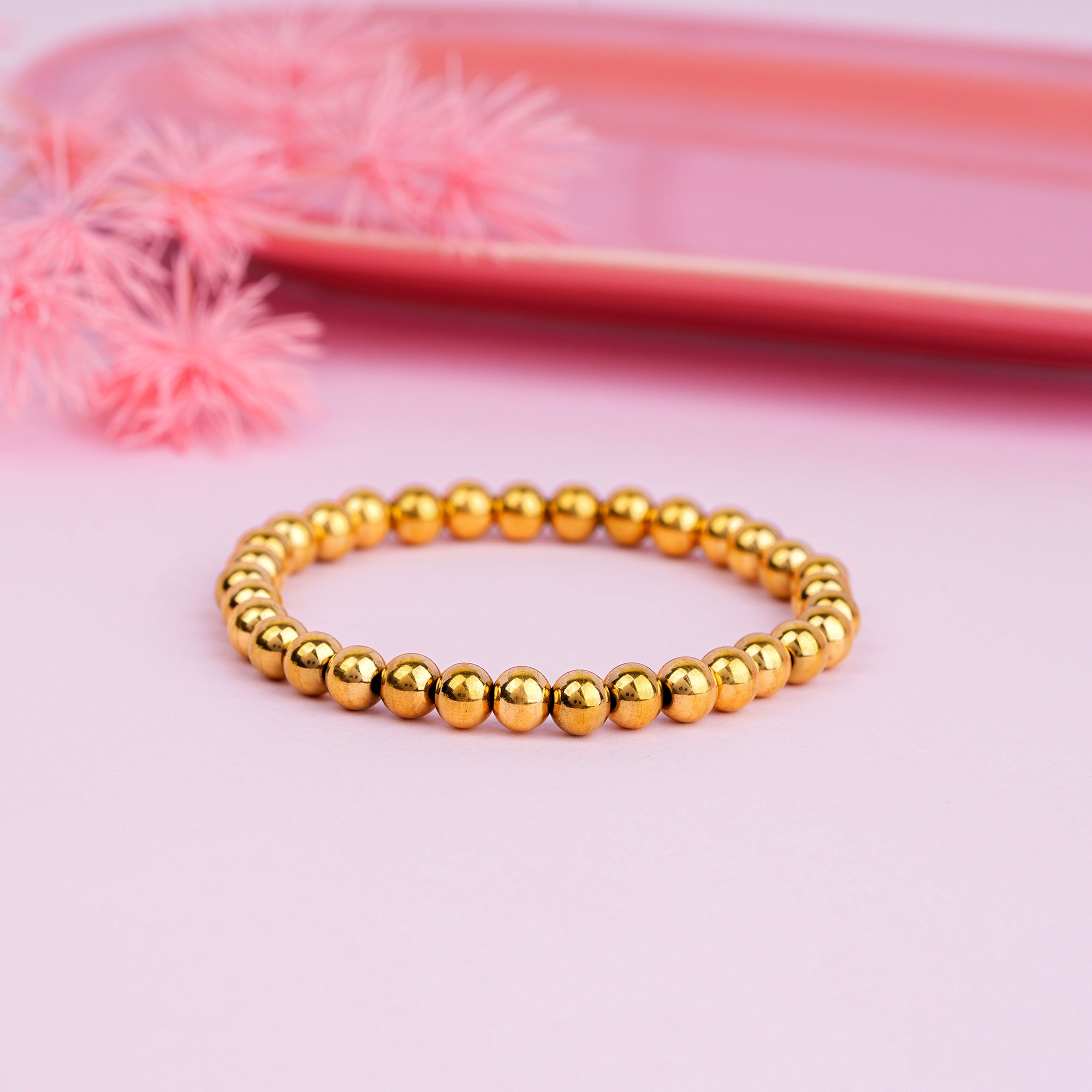 Gold beaded bracelet on a pink background