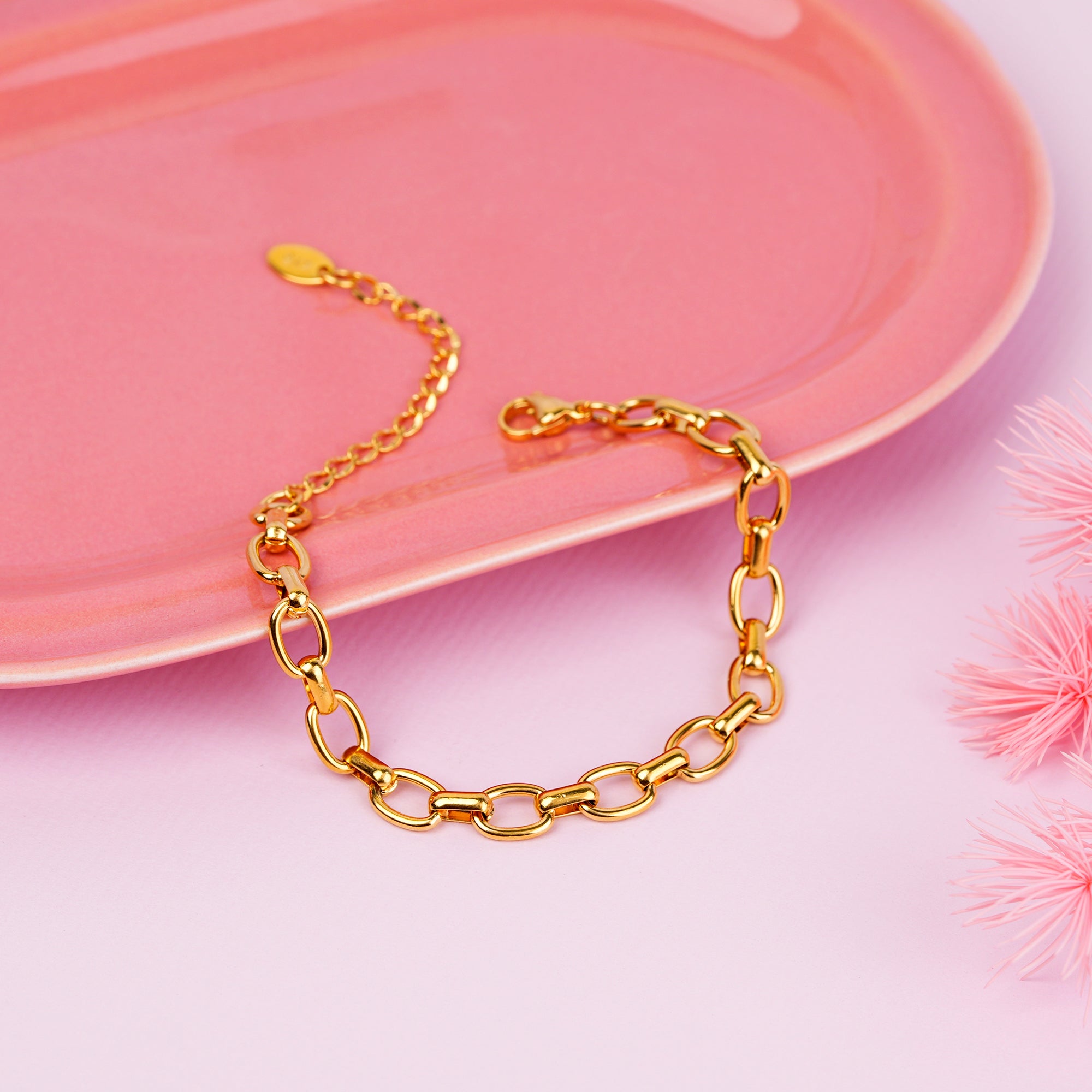 Gold chain bracelet on a pink surface with decorative elements