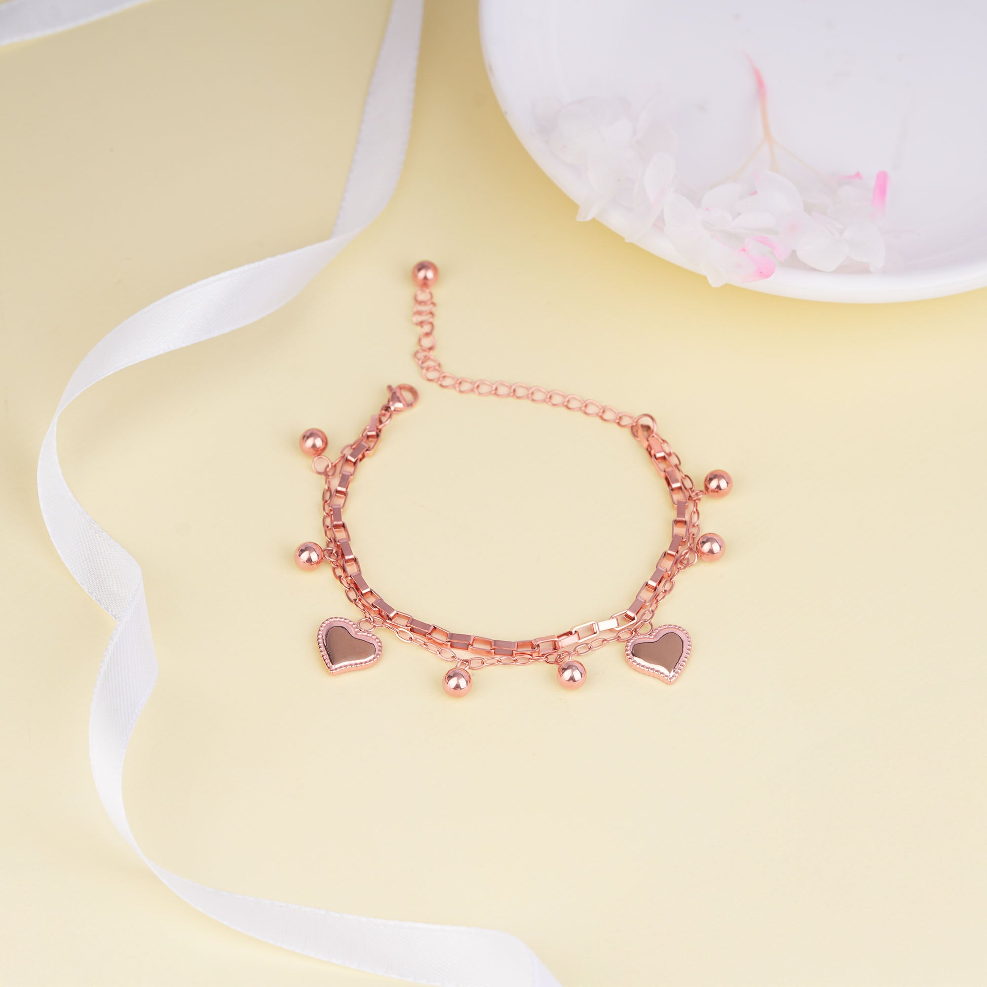 Rose gold bracelet with heart charms on a yellow background