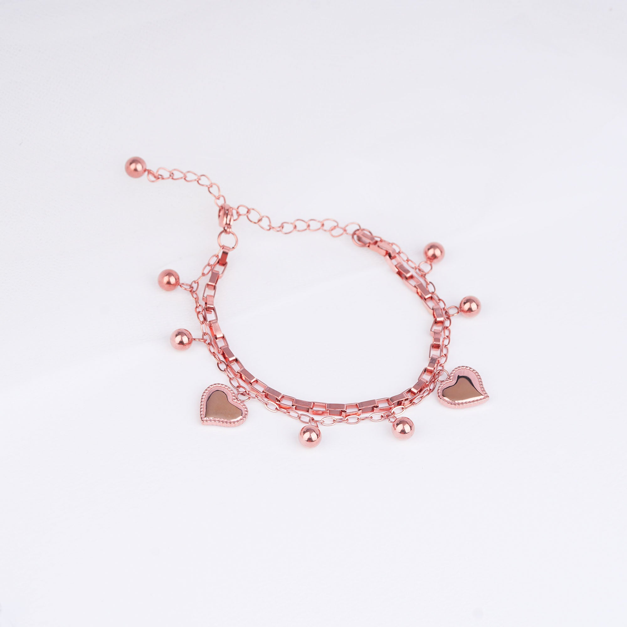 Rose gold bracelet with heart charms on a light pink background