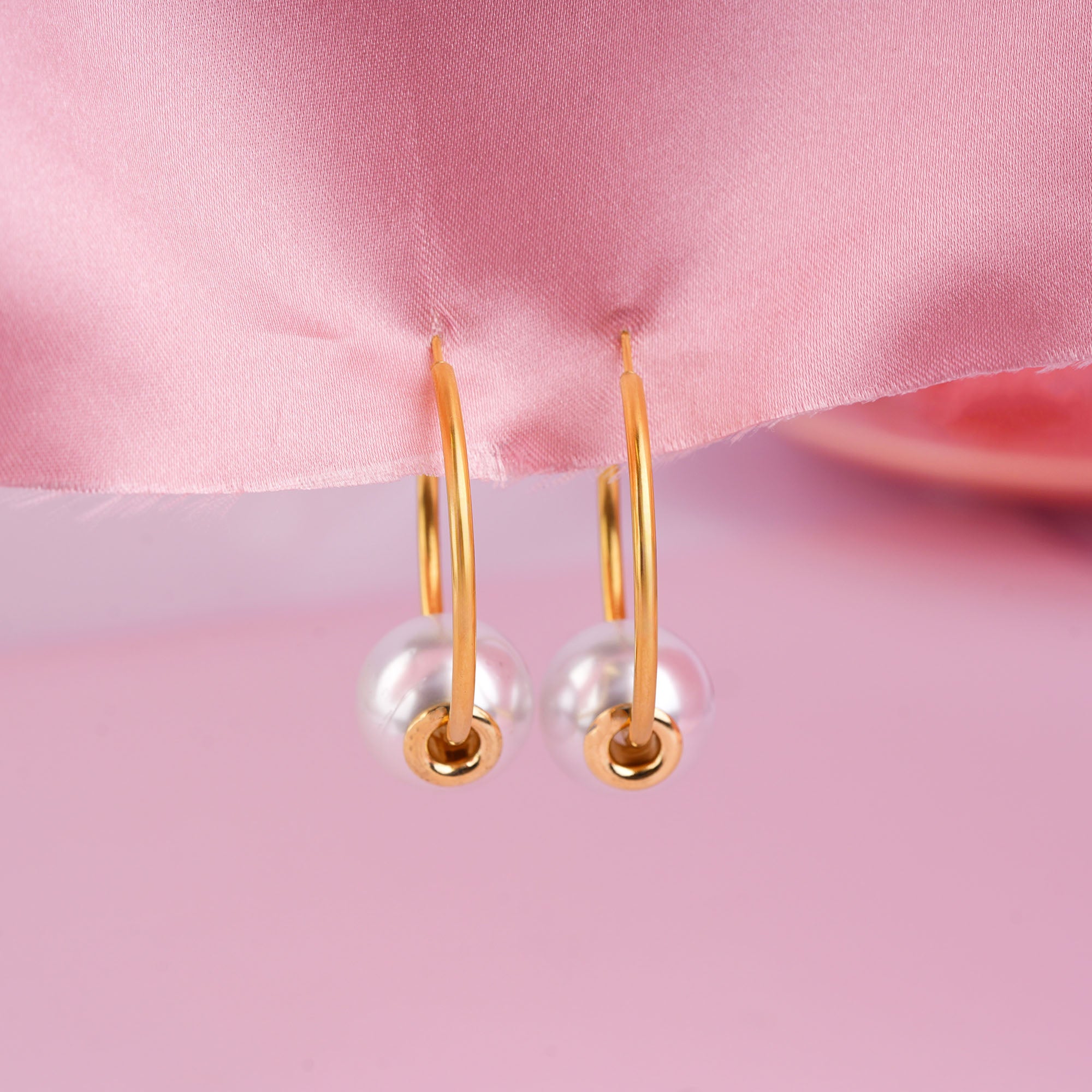 Gold hoop earrings with pearl-like beads on a pink satin background