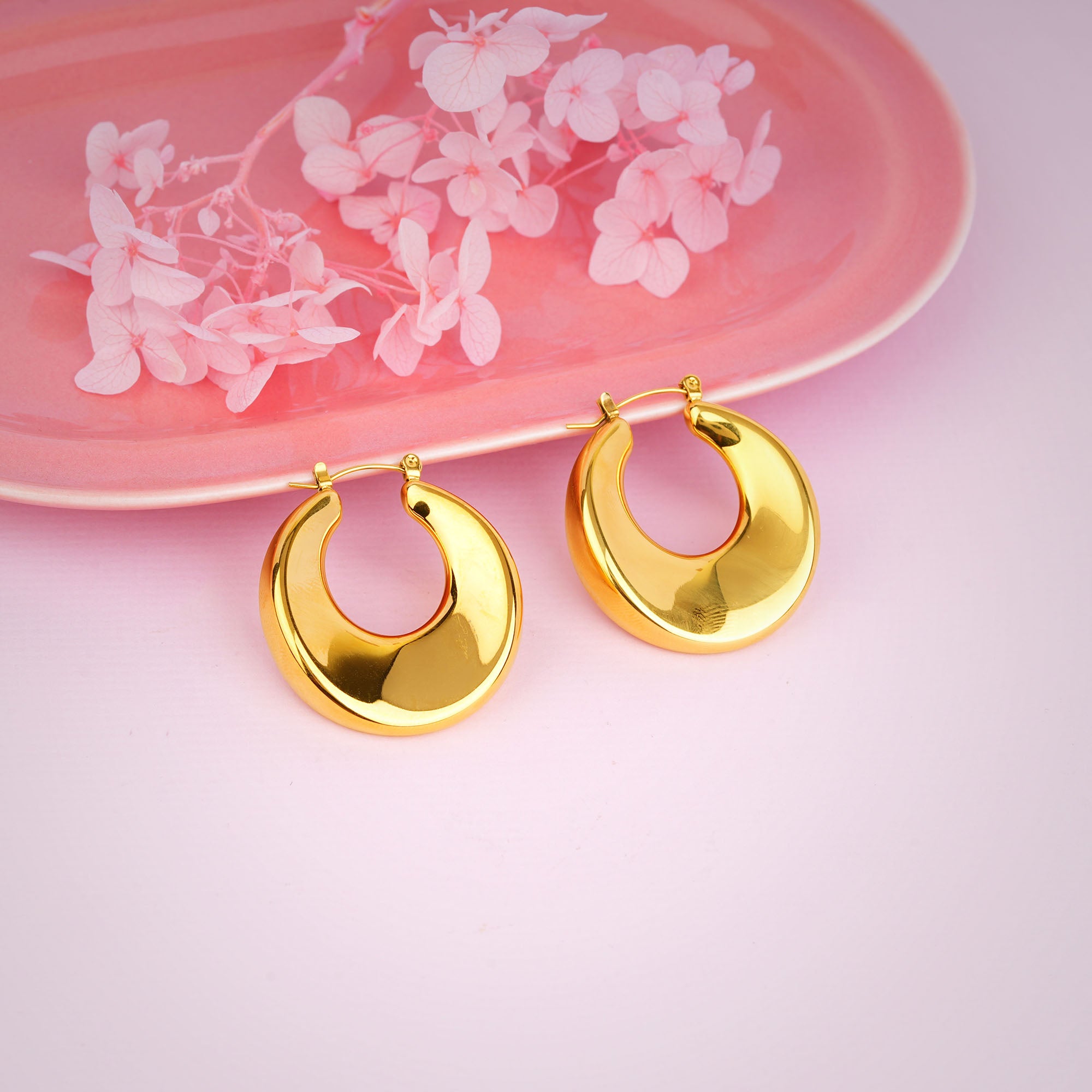 Gold hoop earrings on a pink surface with floral design