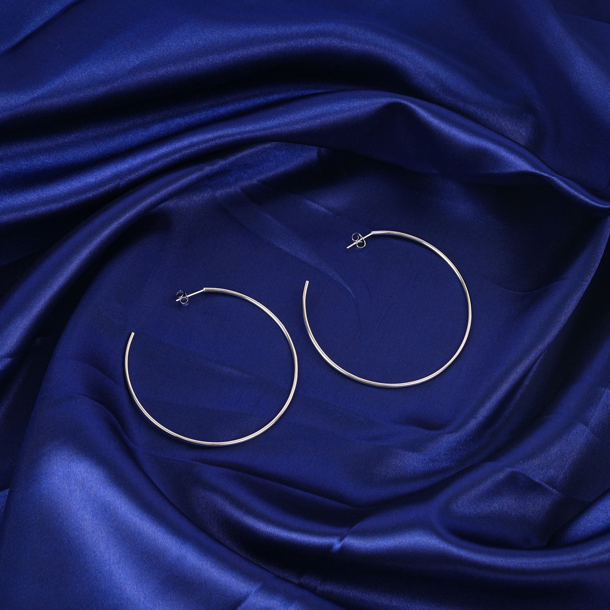 Gold hoop earrings on a blue satin fabric background