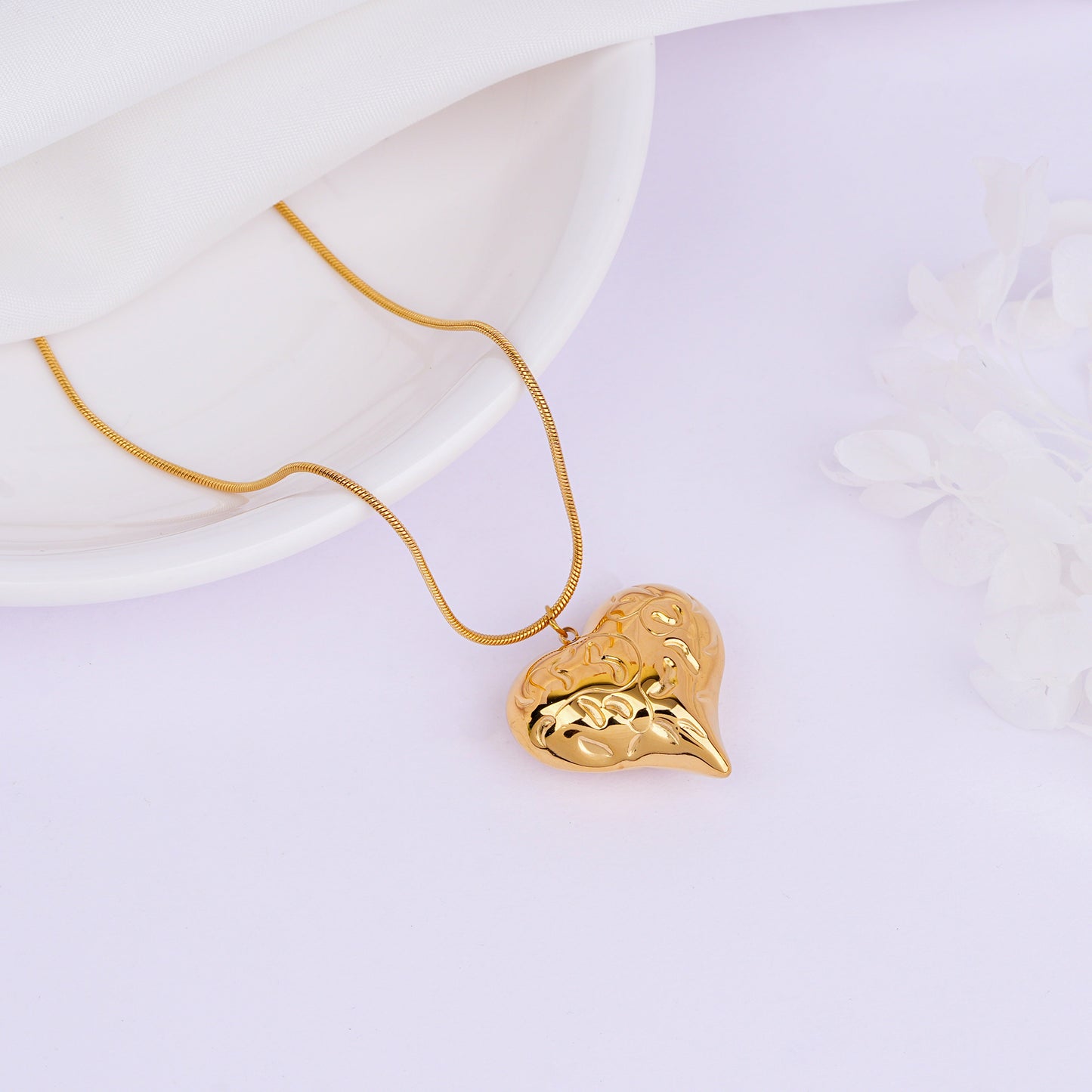 Gold necklace with a heart-shaped pendant on a light purple background