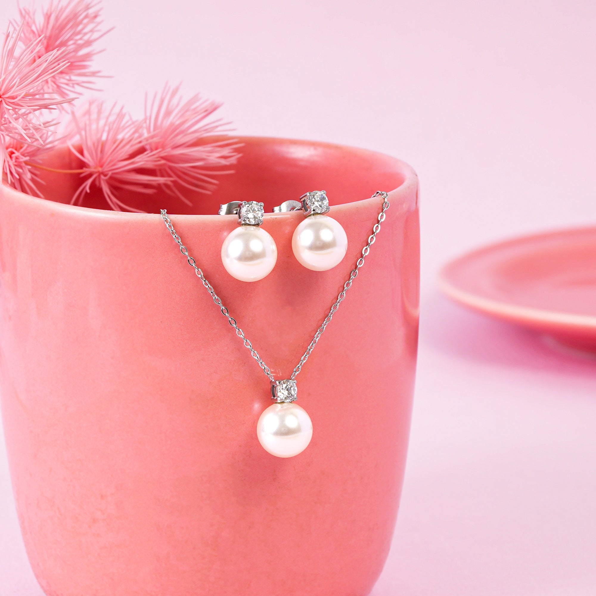Pearl necklace and earrings on a pink cup with pink flowers.