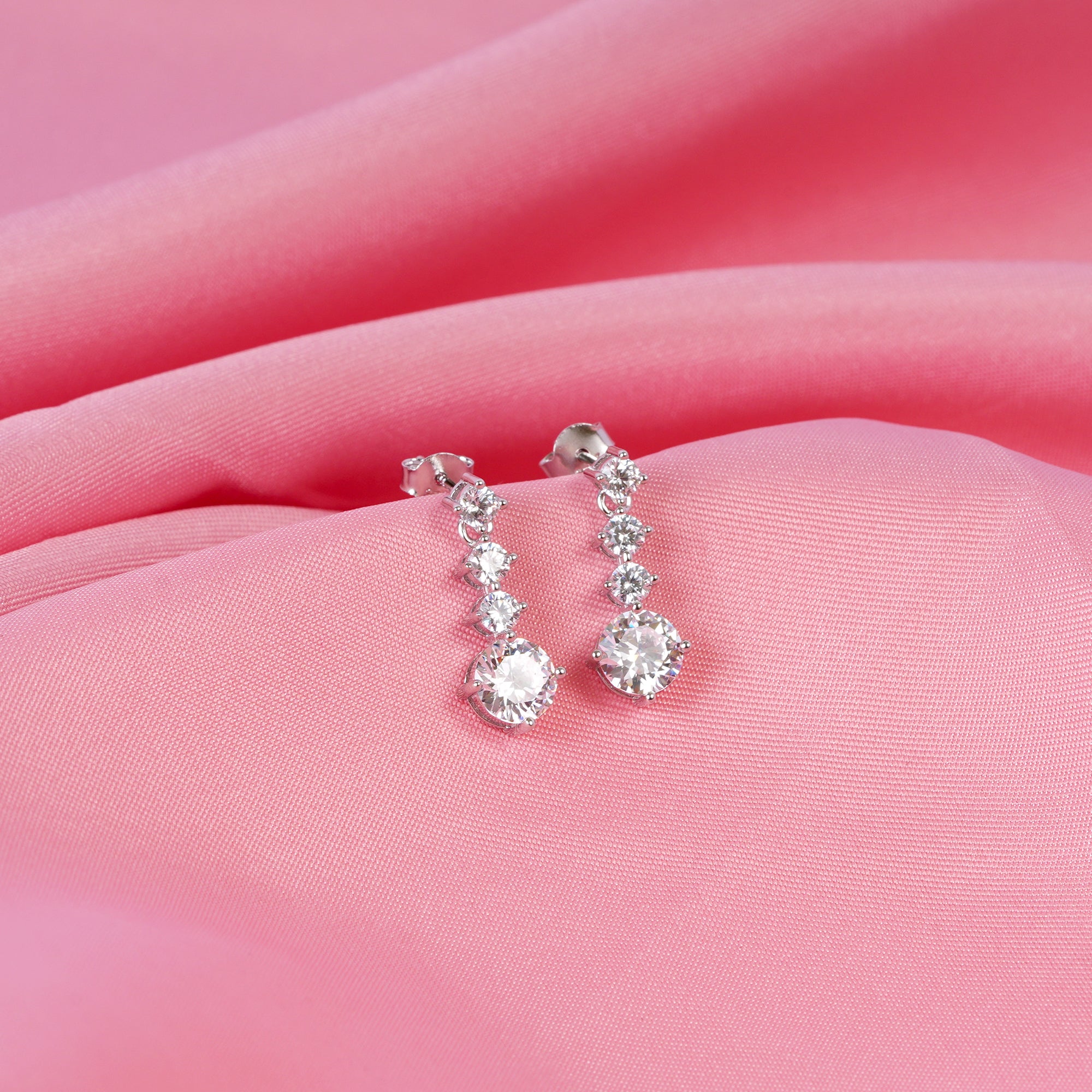 Silver earrings with clear stones on a pink fabric background