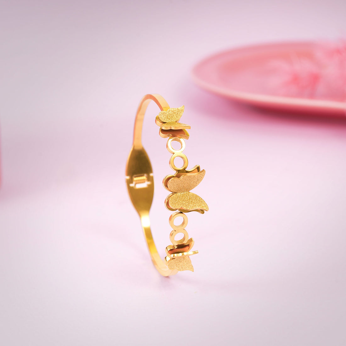 Gold bracelet with butterfly designs on a light pink background