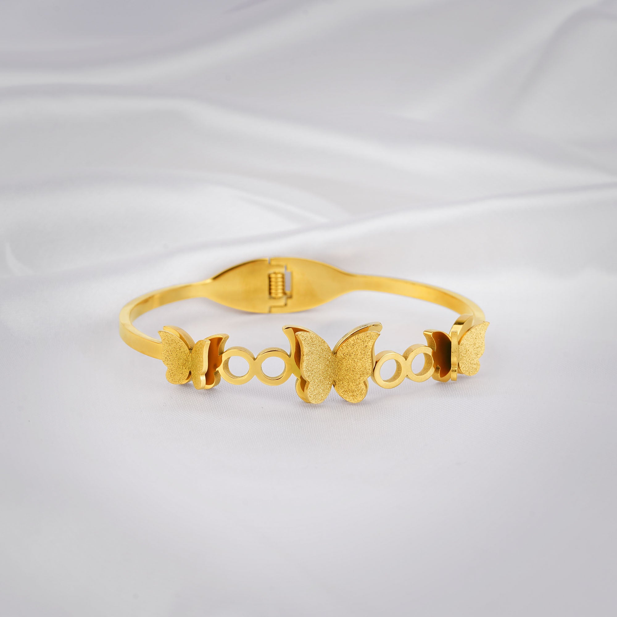 Gold bracelet with butterfly designs on a light gray background