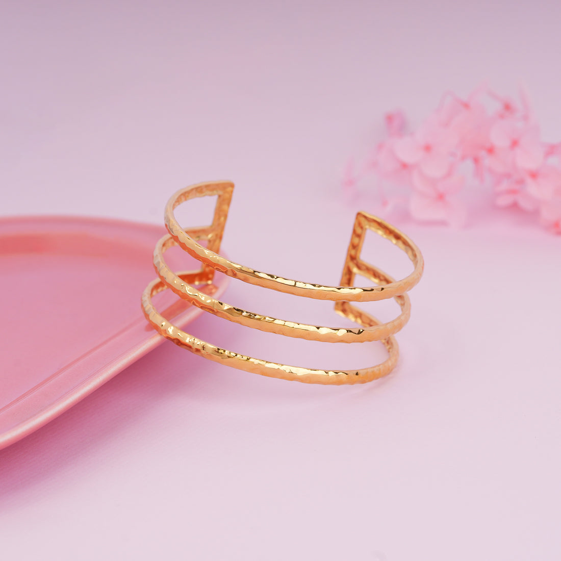Gold bracelet on a pink surface with a soft pink background