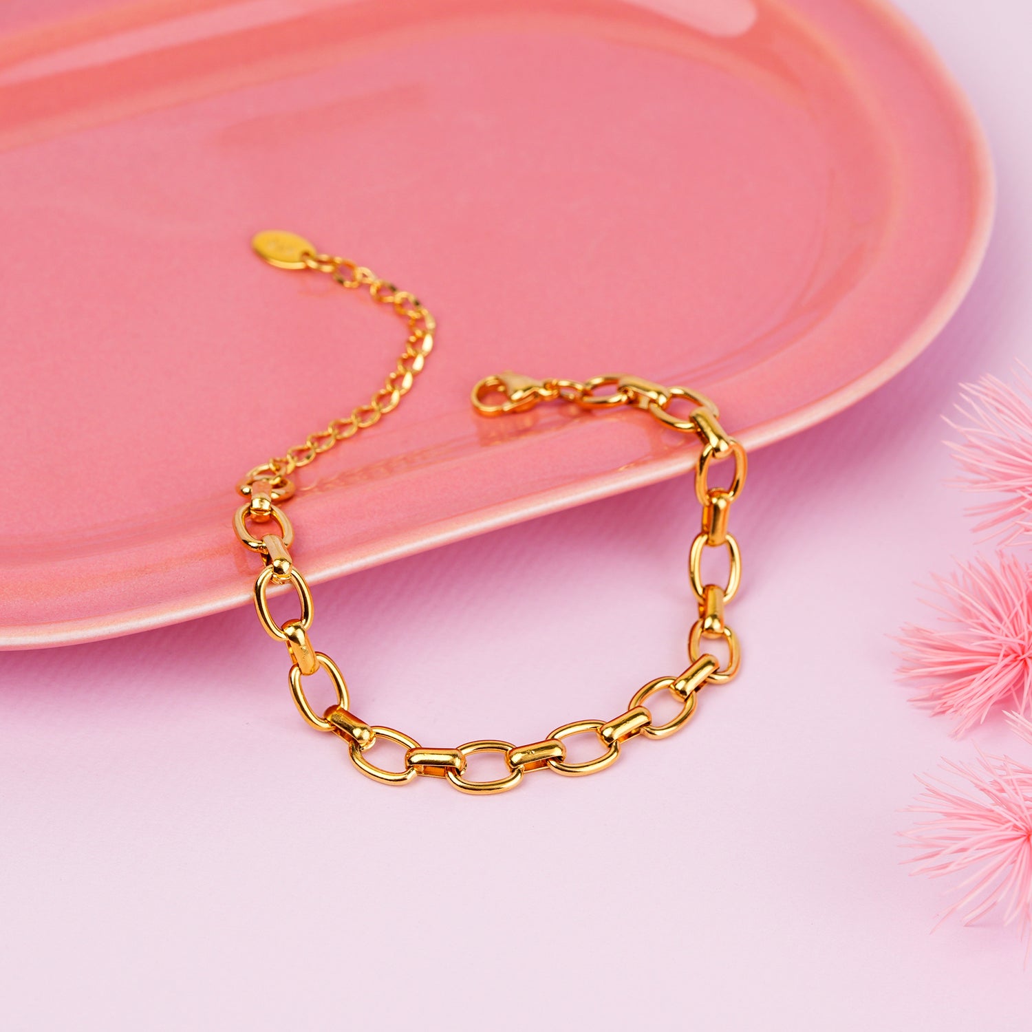 Gold chain bracelet on a pink surface with decorative elements