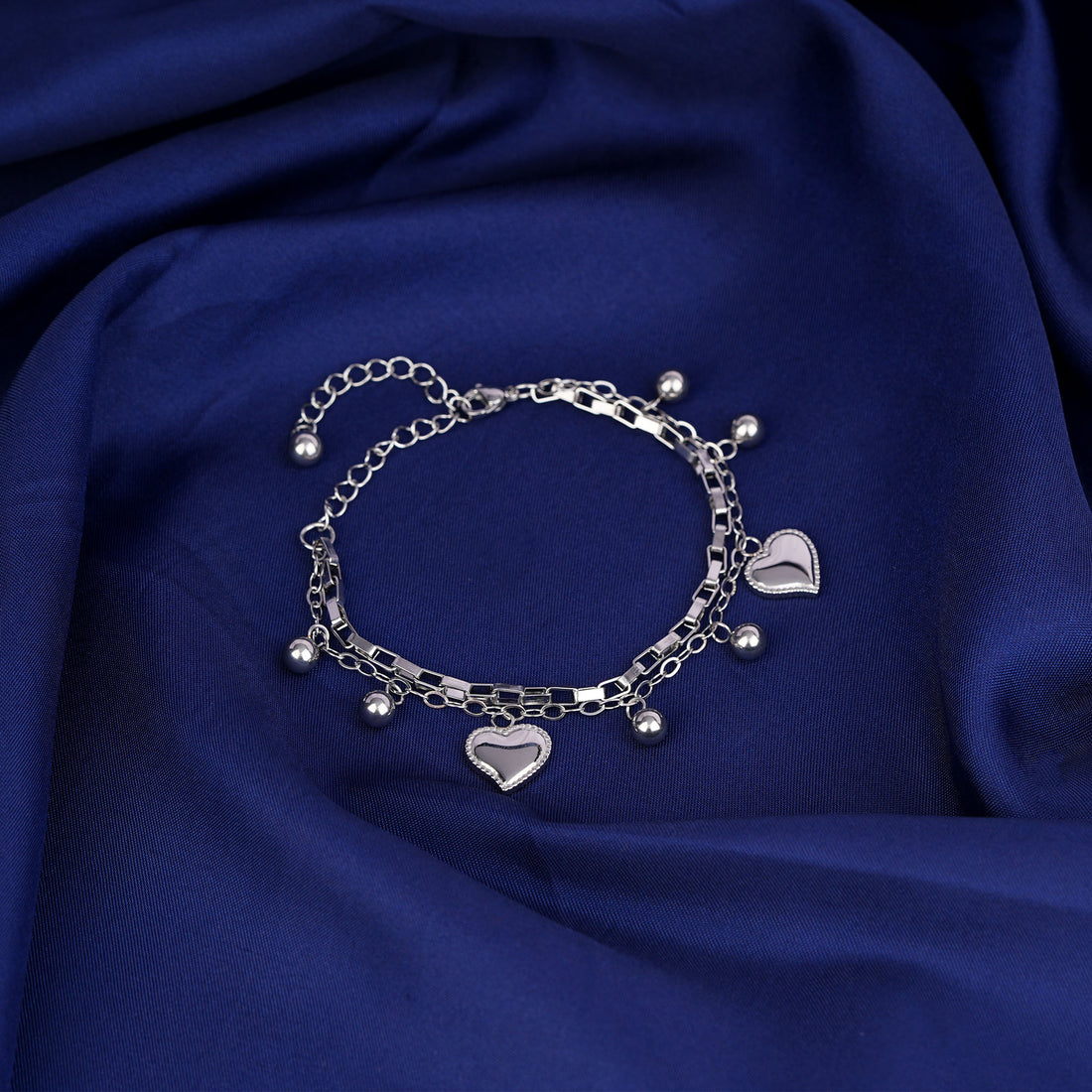 Silver bracelet with heart charms on a blue fabric background