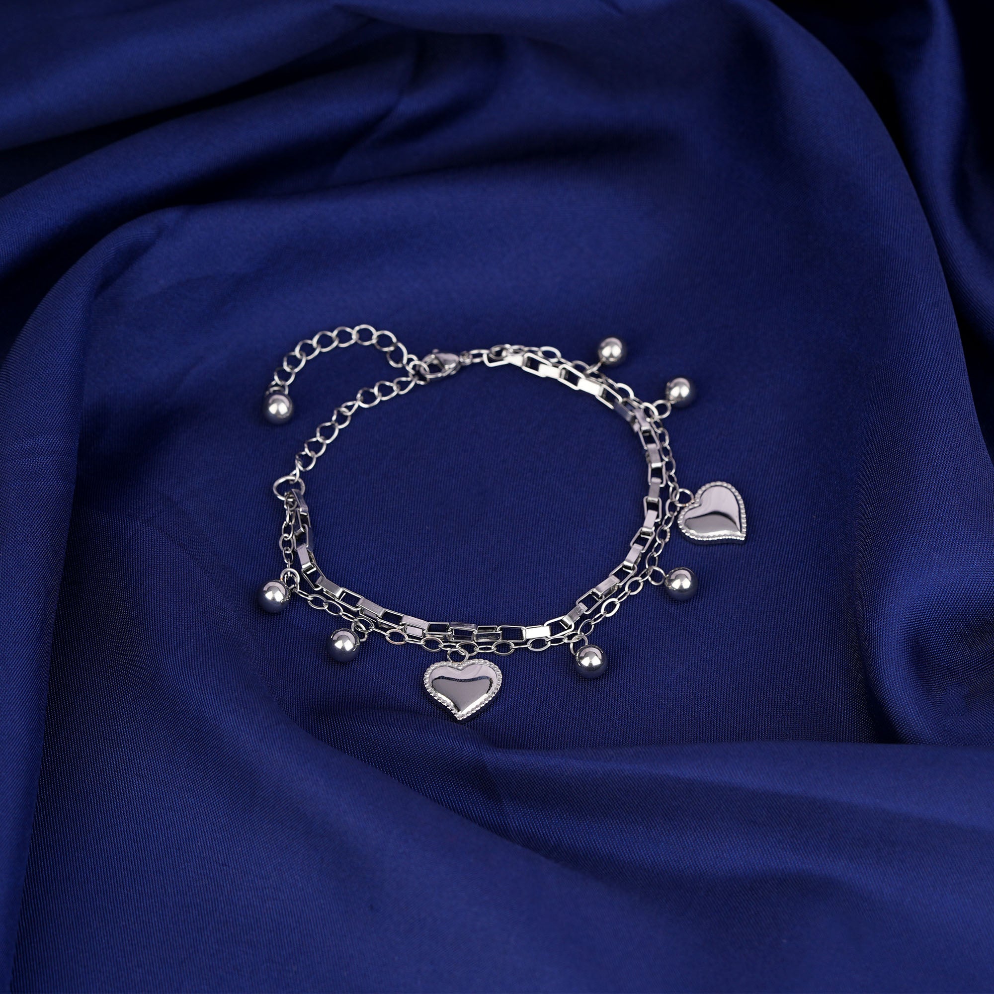 Silver bracelet with heart charms on a blue fabric background