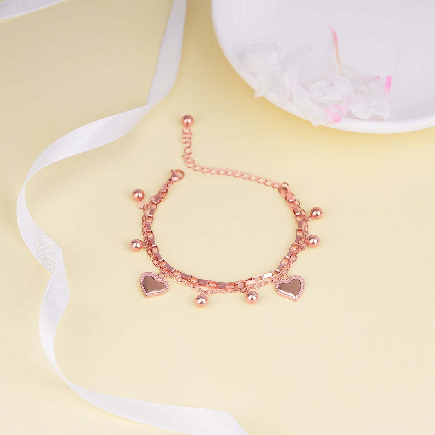 Rose gold bracelet with heart charms on a yellow background