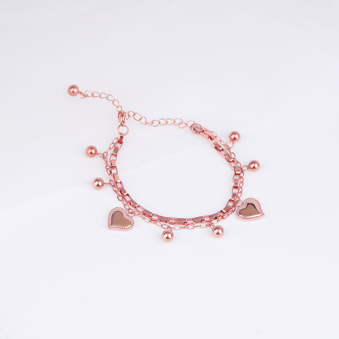Rose gold bracelet with heart charms on a light pink background