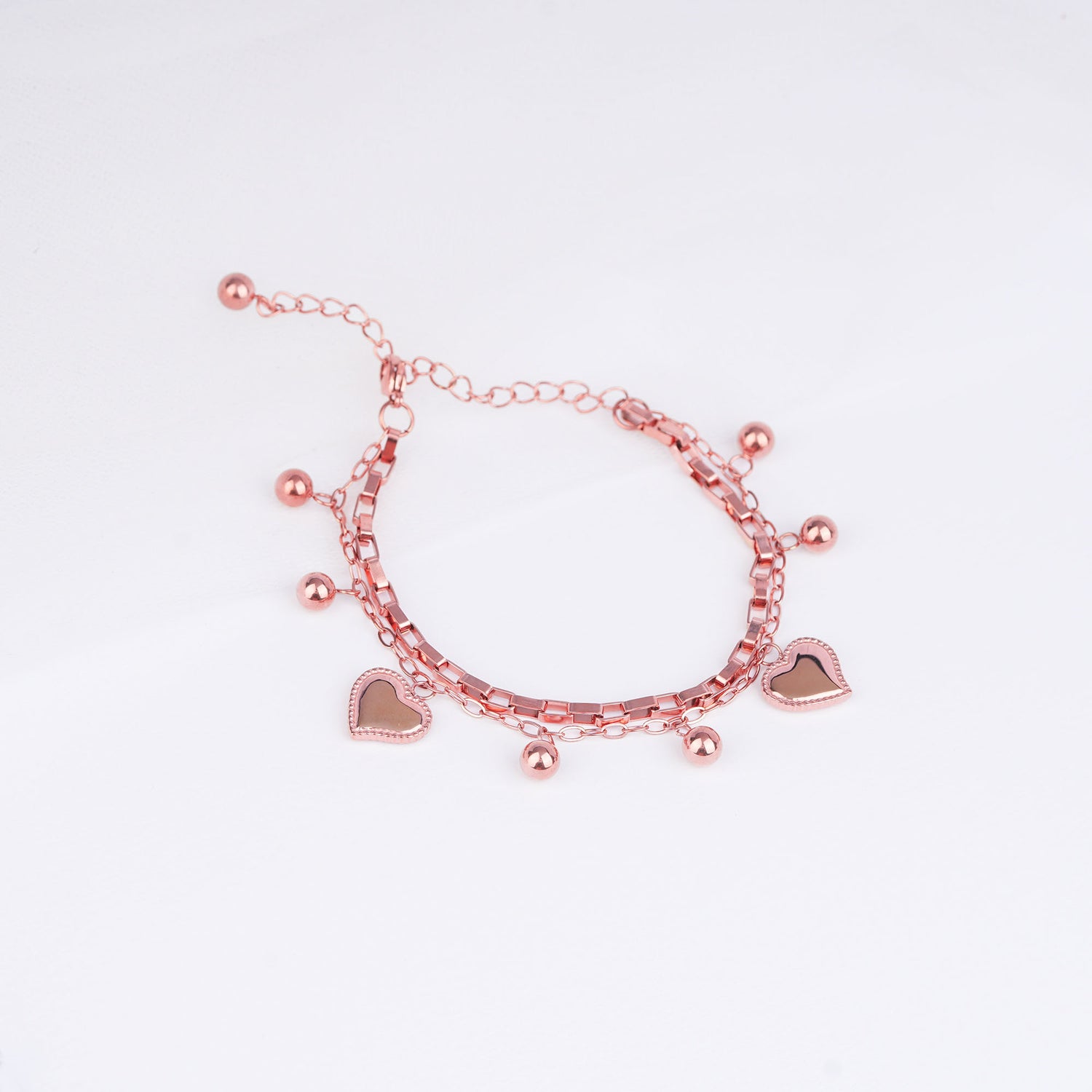 Rose gold bracelet with heart charms on a light pink background
