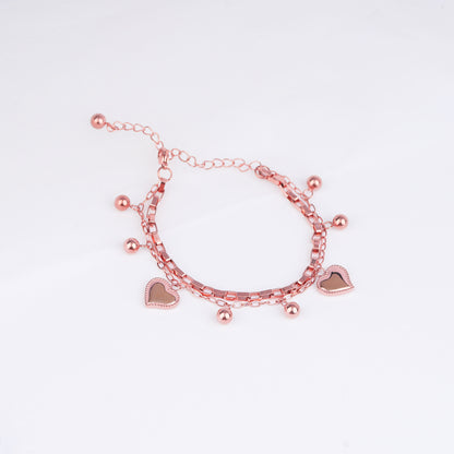 Rose gold bracelet with heart charms on a light pink background