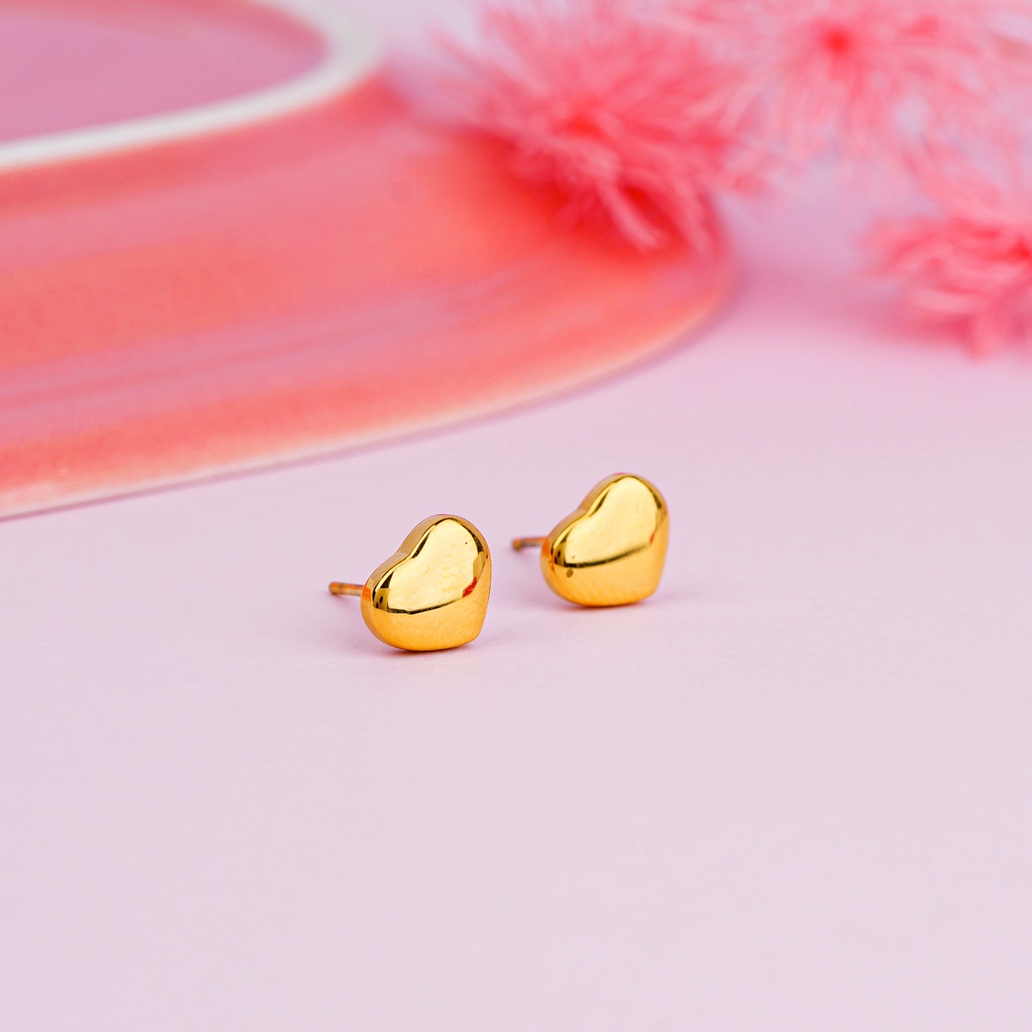 Gold heart-shaped earrings on a pink background