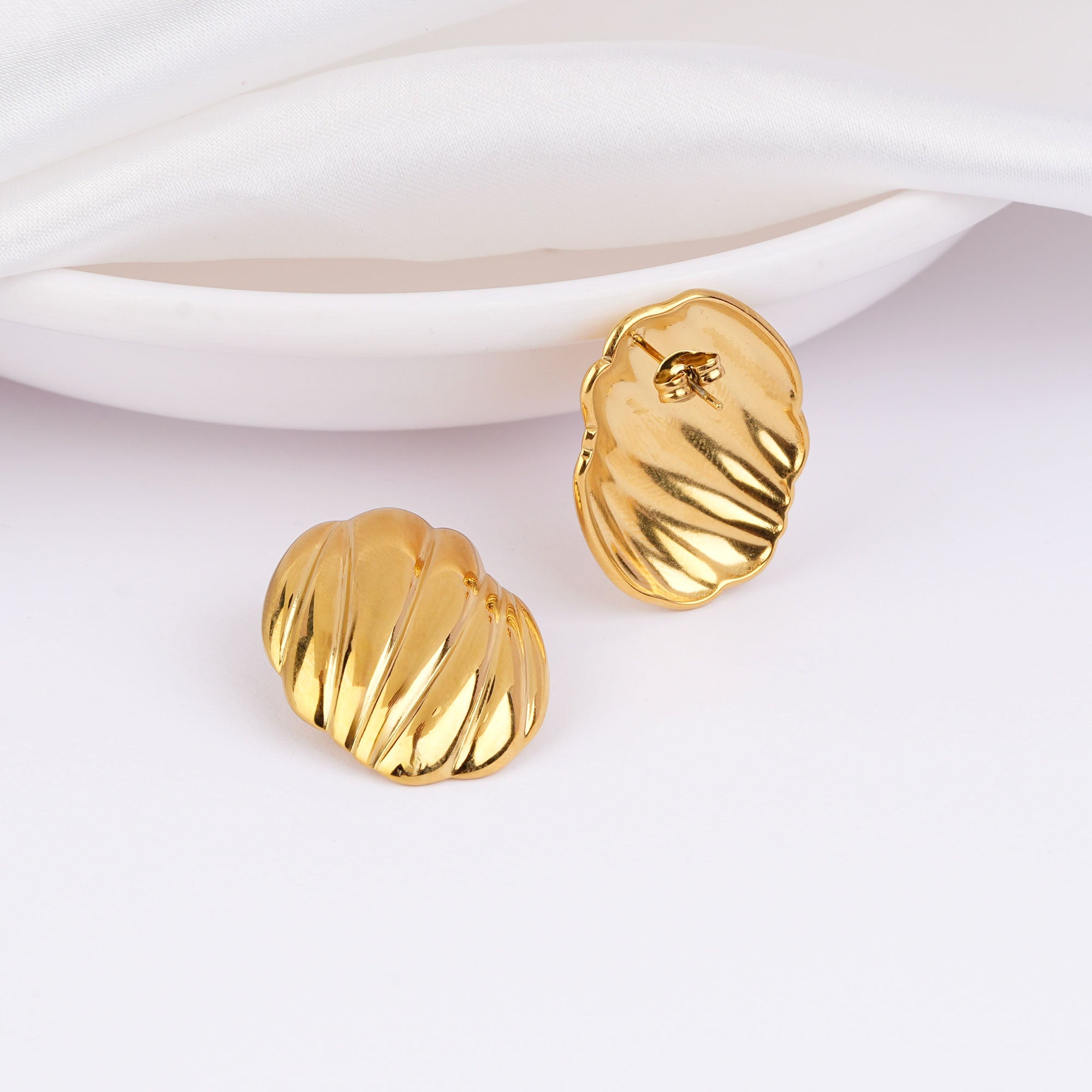 Gold earrings on a white dish with a white background