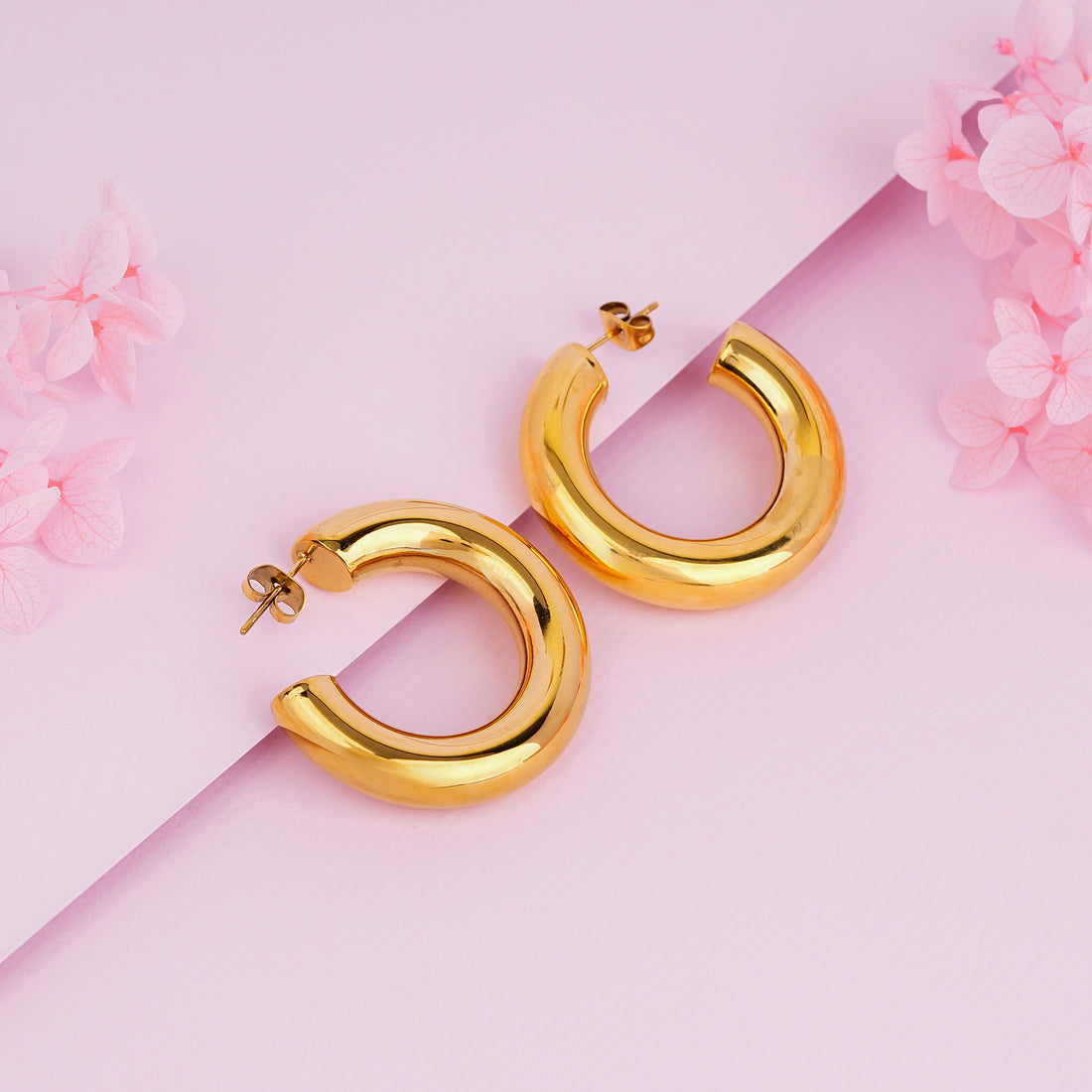 Gold hoop earrings on a pink background with floral elements