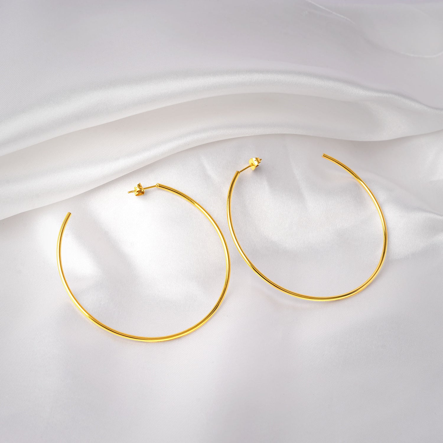 Gold hoop earrings on a white fabric background