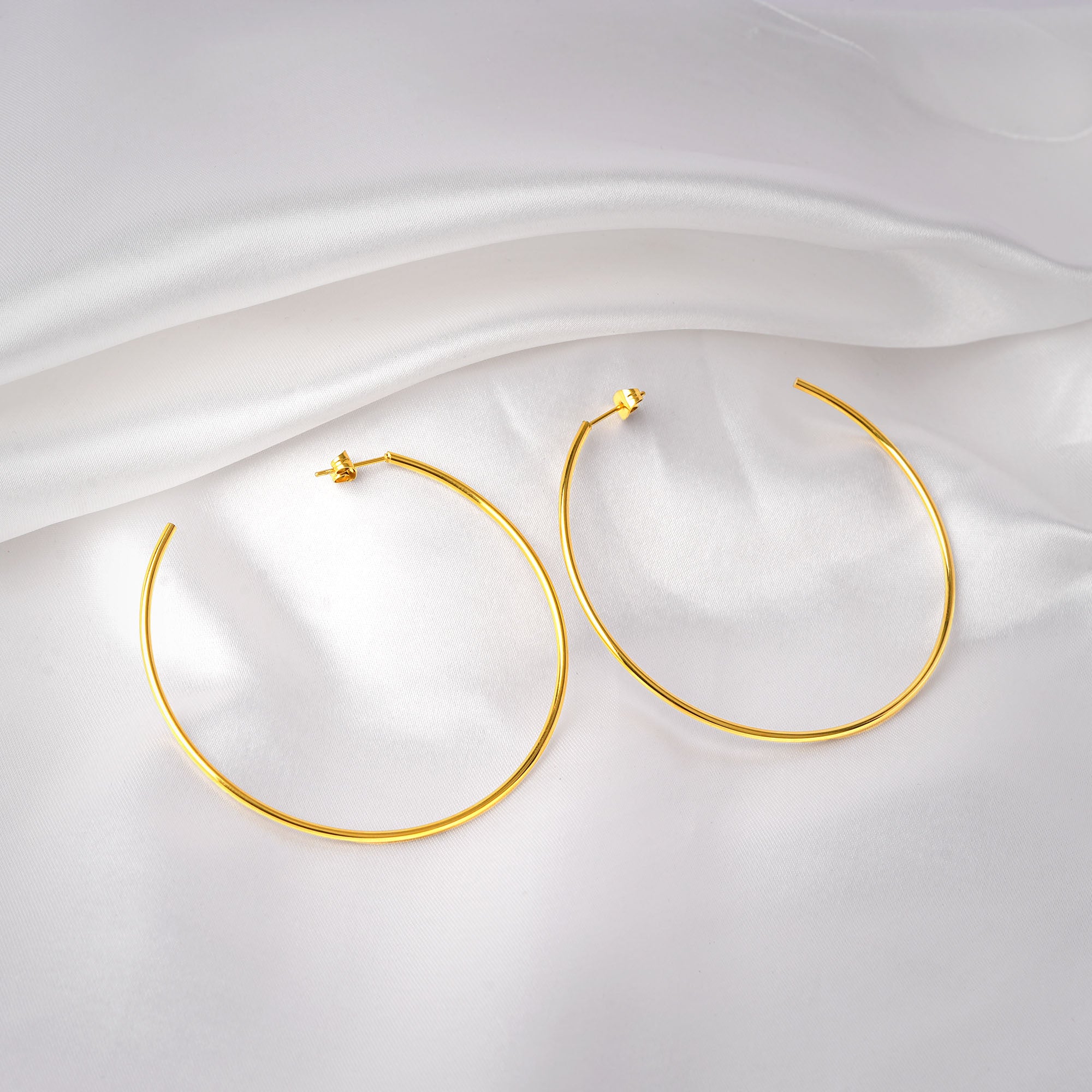 Gold hoop earrings on a white fabric background