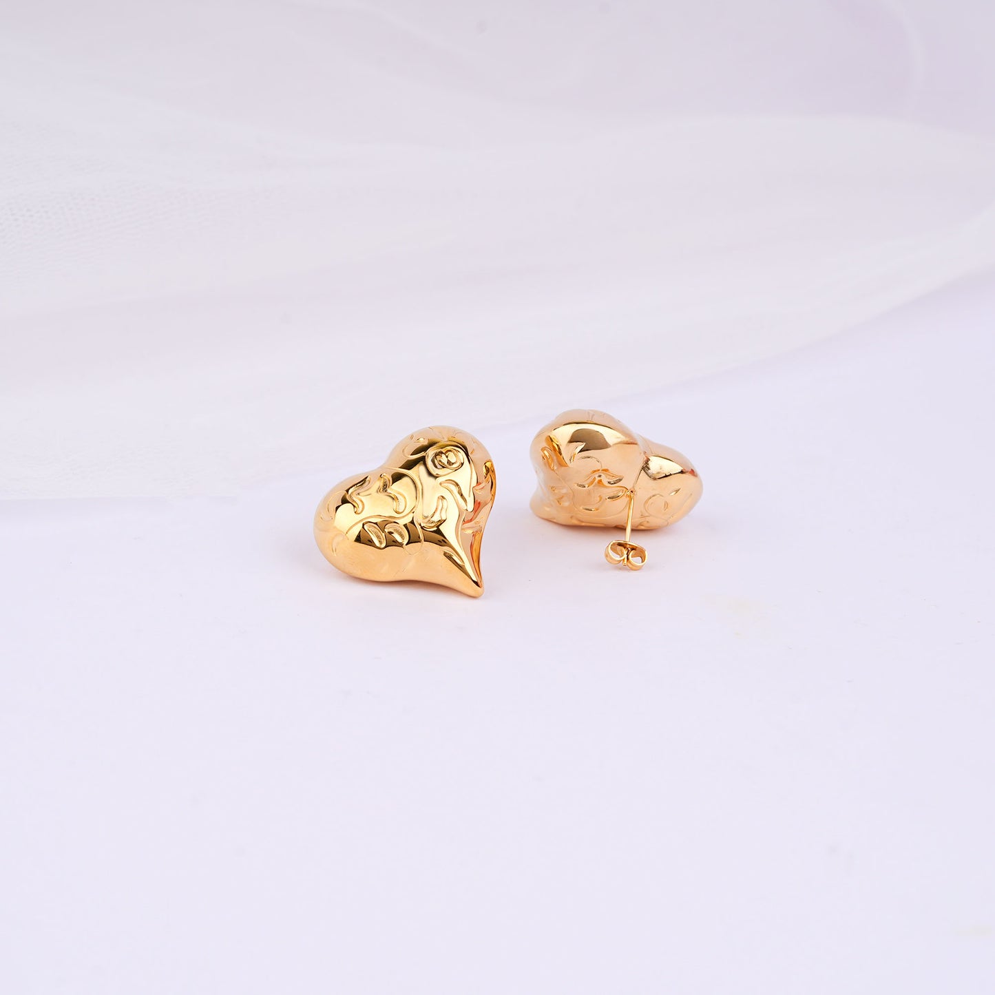Gold heart-shaped earrings on a light gray background