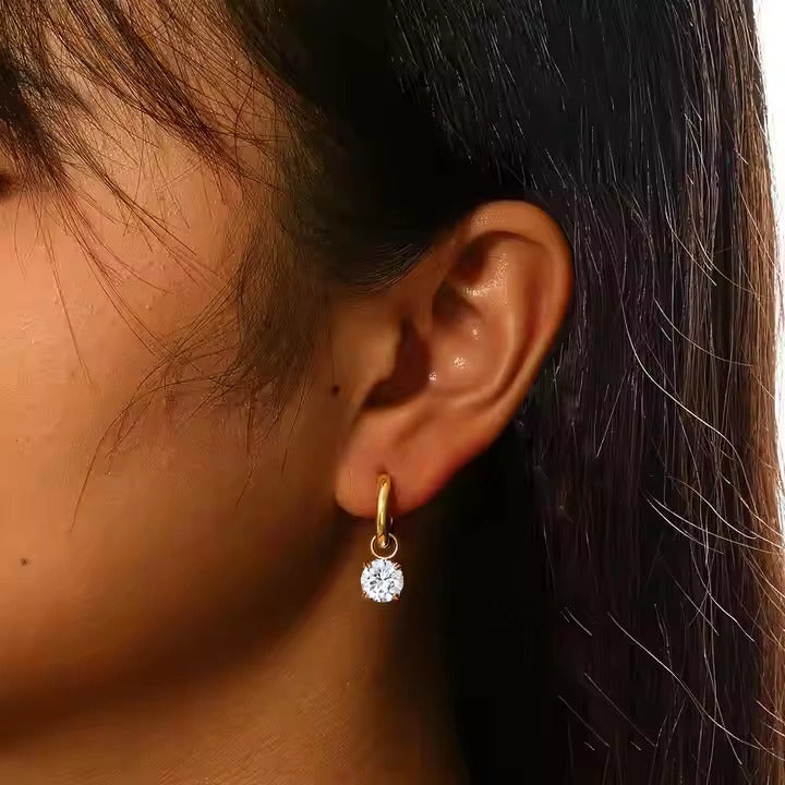 Close-up of an ear wearing a gold earring with a clear gemstone.