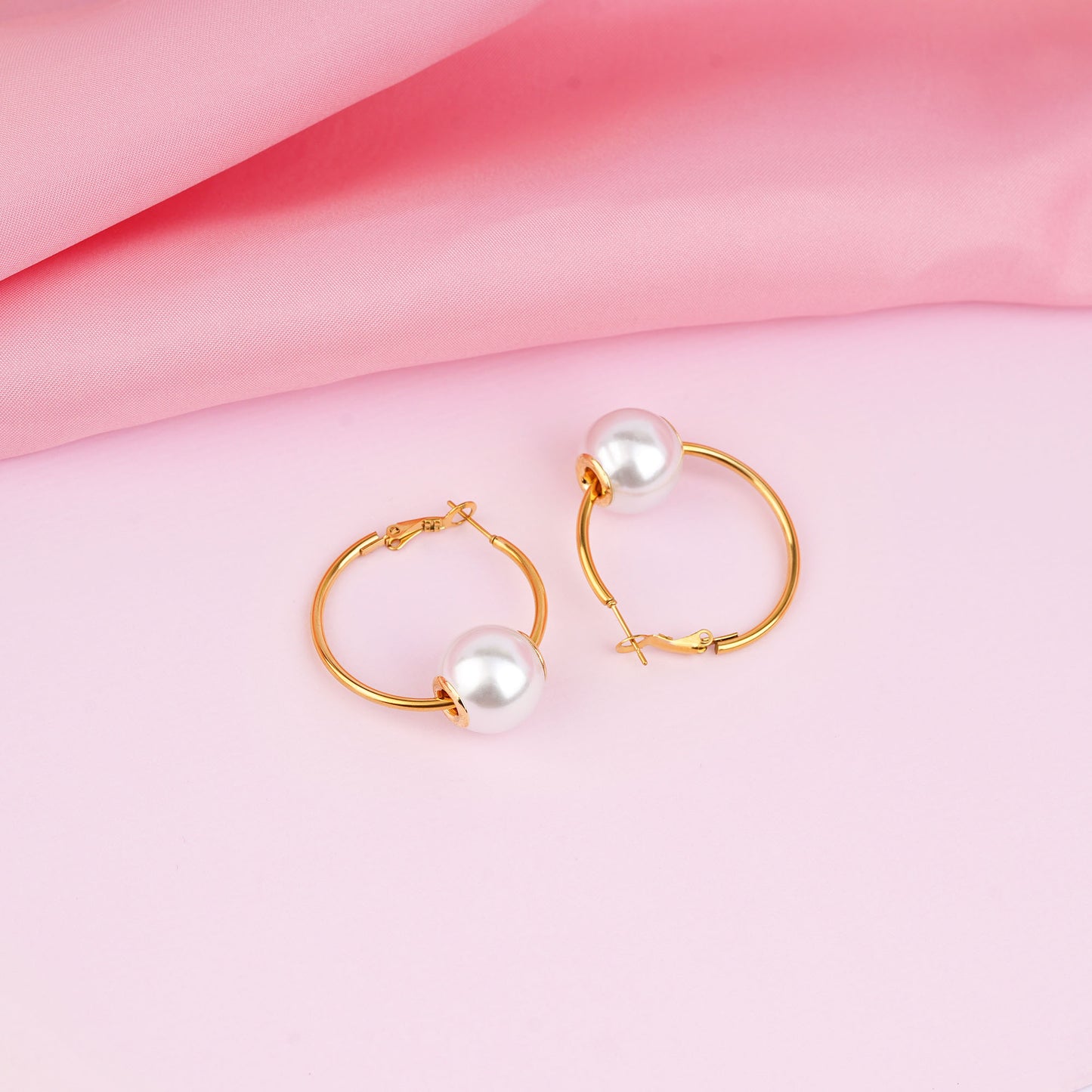 Gold hoop earrings with pearls on a pink fabric background