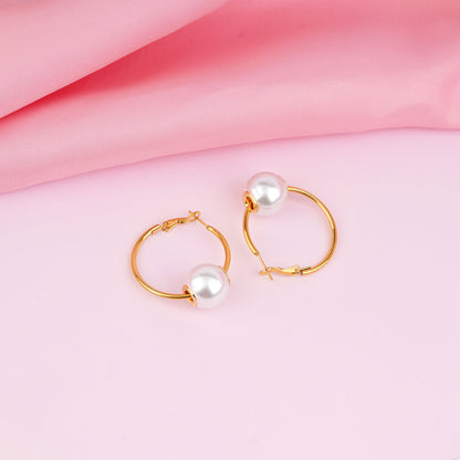 Gold hoop earrings with pearls on a pink fabric background