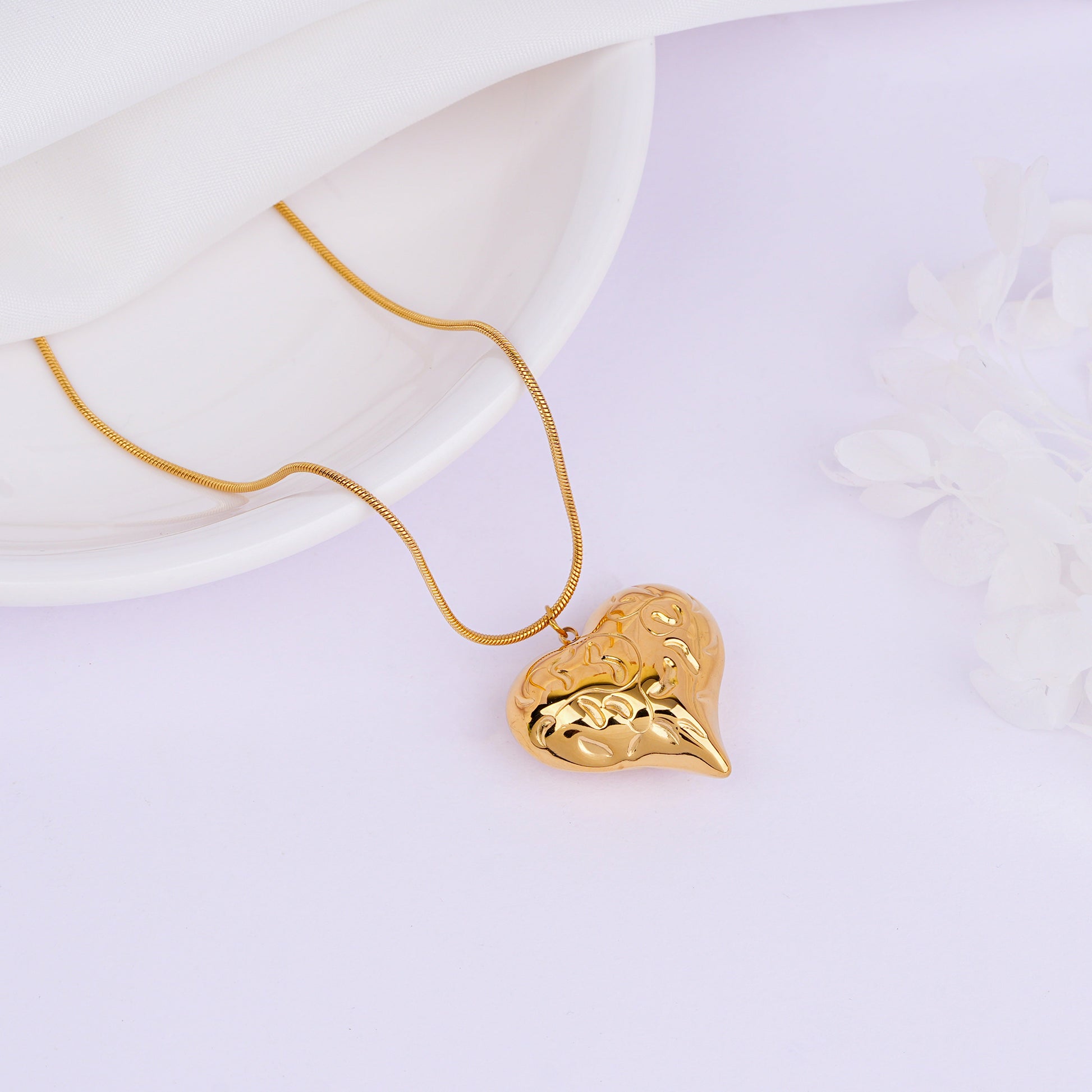 Gold necklace with a heart-shaped pendant on a light purple background