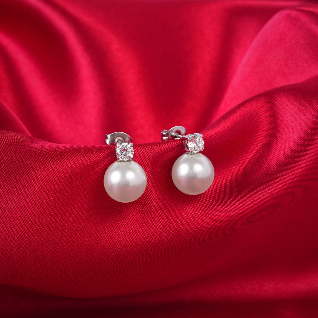 Pearl earrings with small diamonds on a red satin background