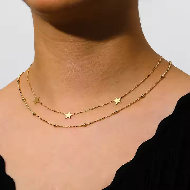 Gold necklace with star pendants on a person's neck against a neutral background