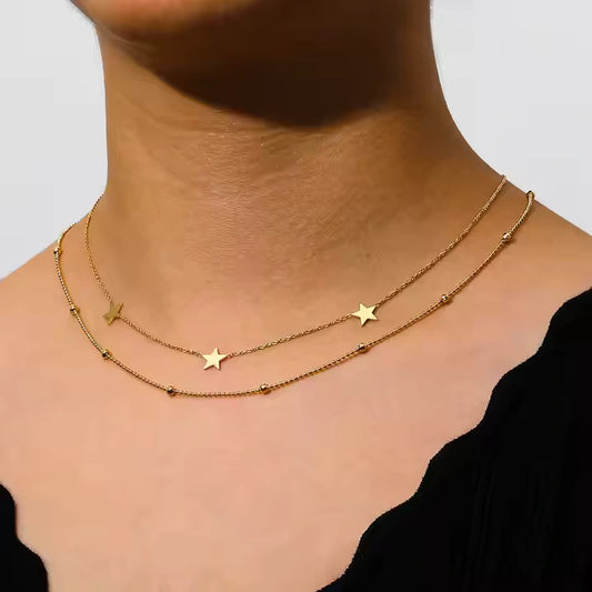 Gold necklace with star pendants on a person's neck against a neutral background
