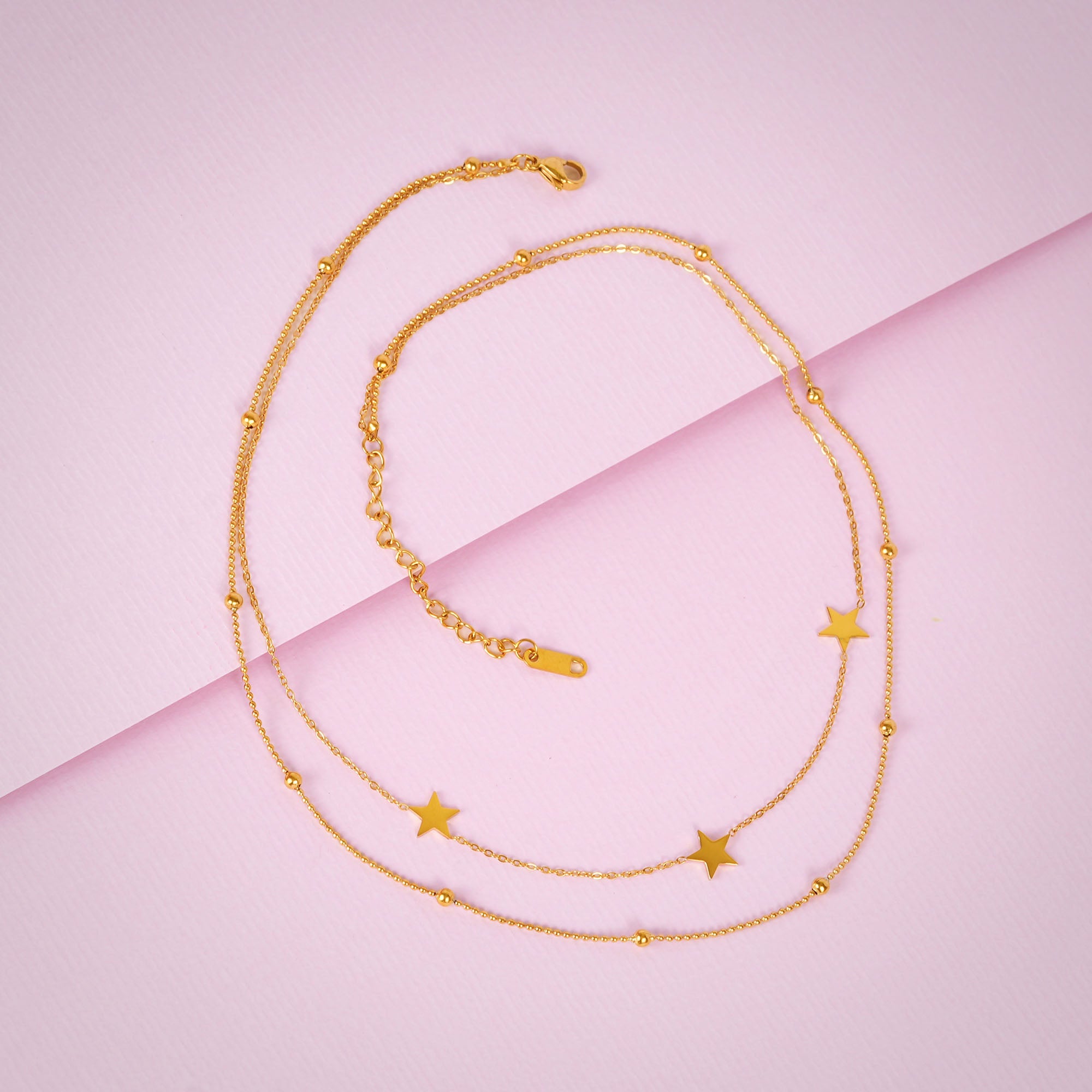 Gold necklace with star pendants on a pink background