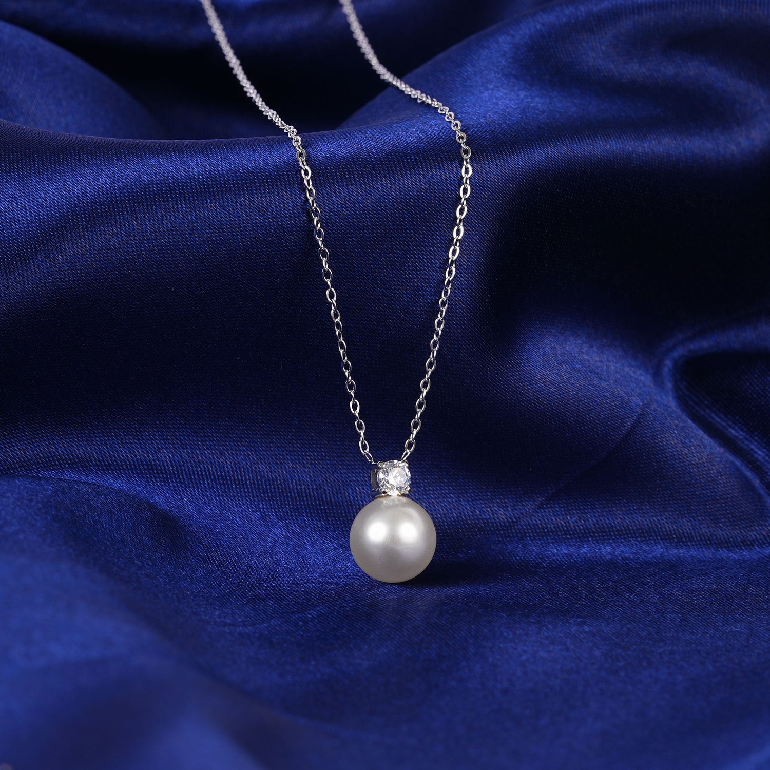 Pearl necklace with a silver chain on a blue fabric background