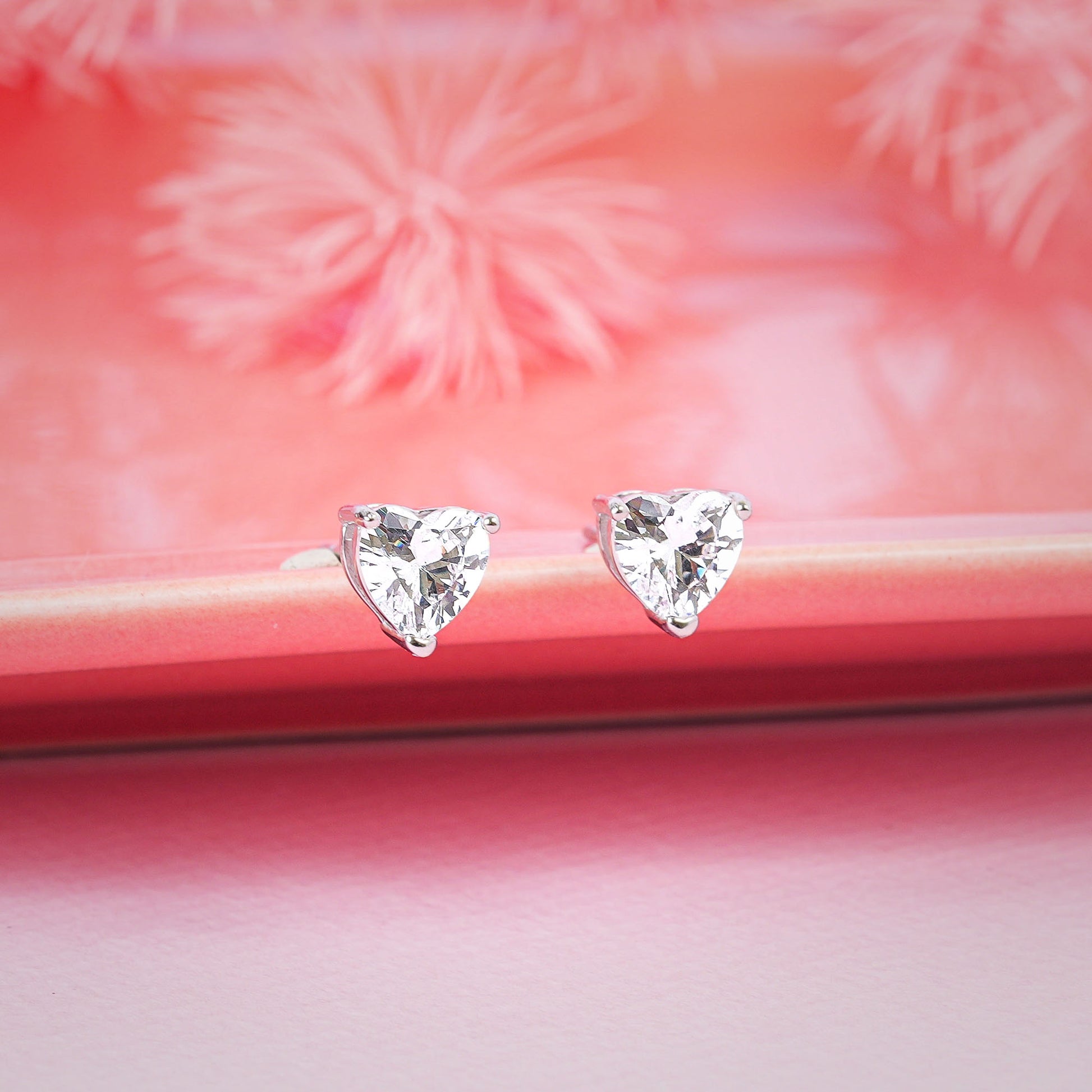 Heart-shaped diamond earrings on a pink surface with floral background