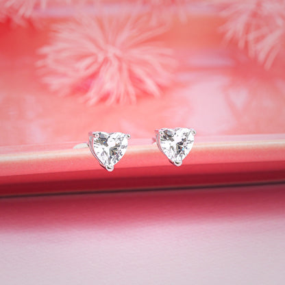 Heart-shaped diamond earrings on a pink surface with floral background