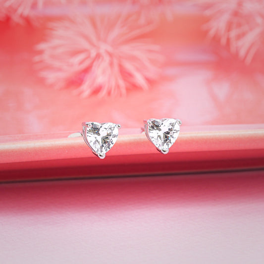 Heart-shaped diamond earrings on a pink surface with floral background