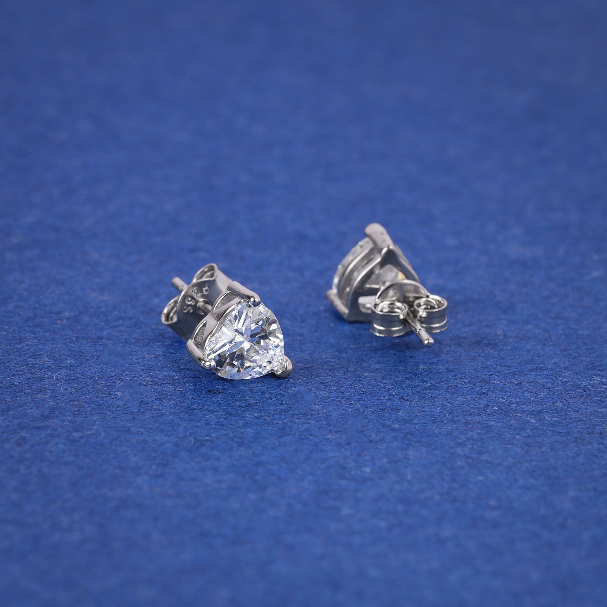 Pair of silver heart-shaped gemstone stud earrings on a blue background