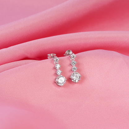 Silver earrings with clear stones on a pink fabric background